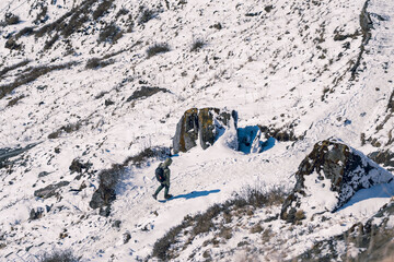 An aerial from behind a man walking on a snowy mountain during the Mardi Himal Trek, Nepal. There are footprints along the path, with bushes on both sides. Idea for adventure background in soft tones.
