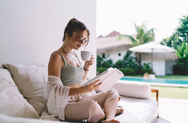 Modern freelancer woman reading tablet and drinking coffee, symbolizing digital autonomy, mobile...