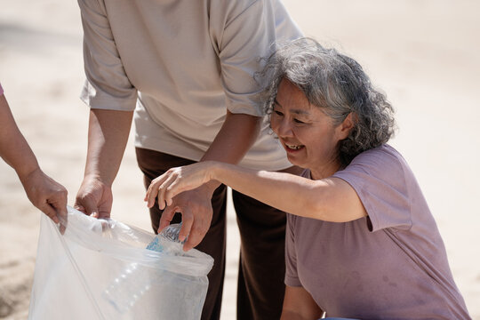 A group of older people are picking up trash on the beach to help keep nature clean and beautiful.