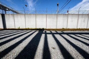 Shadow patterns on gravel under clear sky near concrete fence and security cameras