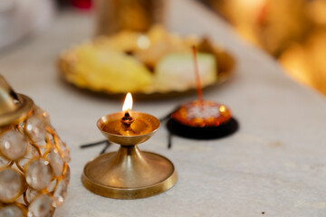 Close-up of a lit brass oil lamp and incense stick on a marble surface during a Hindu prayer...