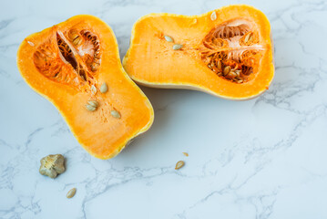 Halved butternut squash with seeds on marble surface.