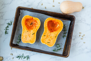 Seasoned butternut squash halves on baking tray with herbs.