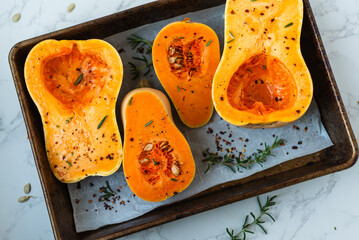Seasoned butternut squash halves on baking tray with herbs.