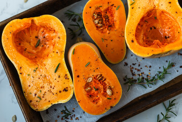 Seasoned butternut squash halves on baking tray with herbs.