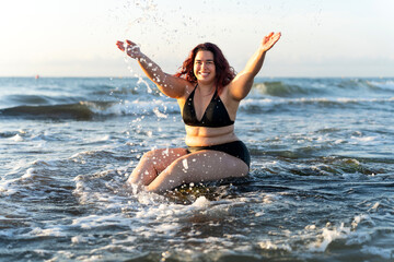 Happy plus size woman splashing water at sunrise beach