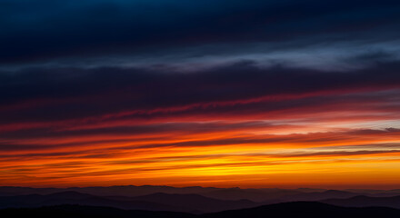 Dramatic mountain range silhouetted against a vibrant, fiery sunset sky