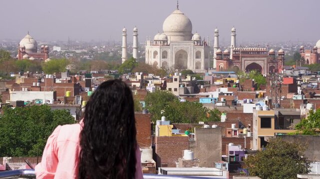 Young Indian woman looking over the Agra cityscape at the white marble monument Taj Mahal the symbol of everlasting love and the seven wonders of the world