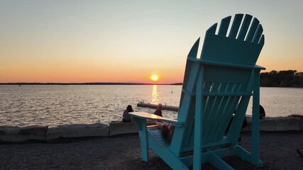 Large turquoise Adirondack chair overlooking serene lake at sunset with people enjoying the peaceful atmosphere