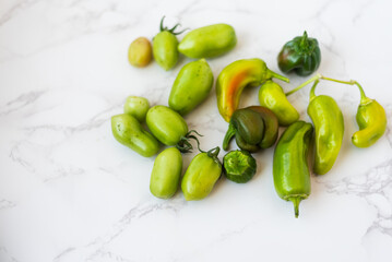 Green tomatoes and green peppers on marble with cutting board.