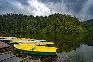 dock with boats on Red lake, Romania, against forested hills and dramatic rainy sky, beautiful...