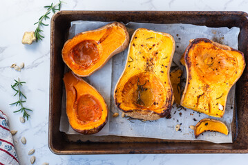 Freshly roasted butternut squash halves with herbs and spices sit on a parchment-lined baking tray, showcasing warm autumn colors and rustic homemade preparation.

