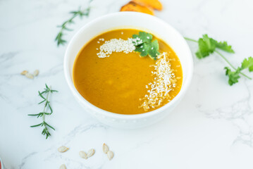 A smooth bowl of butternut squash soup garnished with sesame seeds and fresh cilantro sits on a white marble surface, capturing a light and wholesome seasonal meal.