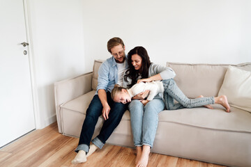 Young parents cradle and tickle daughter in spontaneous moment of laughter, reflecting real-time...