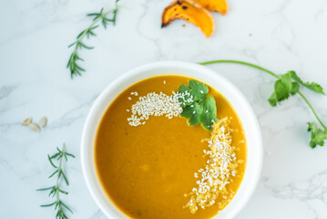 A smooth bowl of butternut squash soup garnished with sesame seeds and fresh cilantro sits on a...