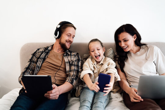 Family smiles while watching phone together, embracing digital closeness and enjoying spontaneous screen-based fun during quality time at home. - Powered by Adobe