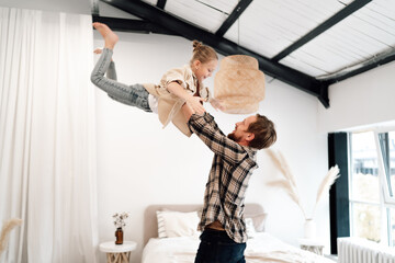 Obraz premium Playful child smiling on father’s shoulders while mother watches, vibrant family energy with focus on joy, connection, and carefree childhood in natural light.