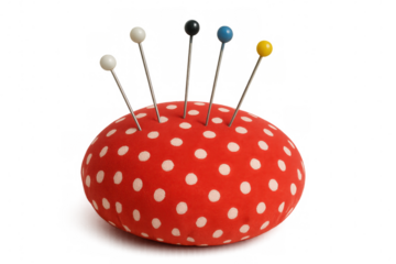 Colorful sewing pins piercing vintage white-dotted red pincushion against transparent backdrop with sharp pointed tips