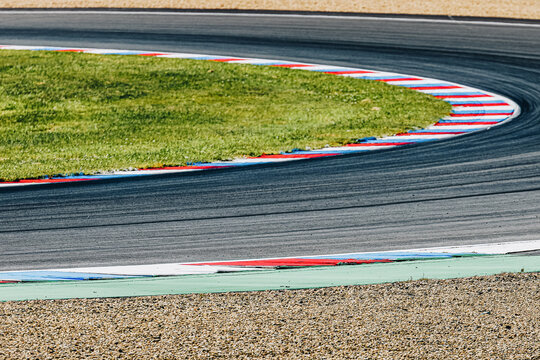 Race track curve with brightly colored curbs. Racing circuit corner, highlighting the red, white, and blue curbs marking the apex and exit of the turn. Asphalt texture and racing line clearly visible