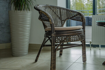 wicker rattan chair indoors. Flower in pot stands in corner