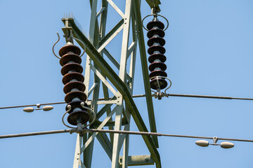 Sunlit high voltage pylon with overhead power lines and insulators  under a blue summer sky....