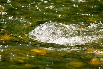 Close up of little rapid in a clear river with beautiful green water. Water texture with bubbles on the rapid.