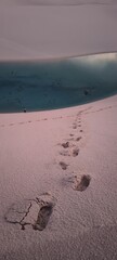 Lençóis Maranhenses, Santo Amaro. Footprints in the white sand leading to a crystal clear lagoon in desert landscape at sunset. A lone person walks in the distance, conveying a sense of adventure.