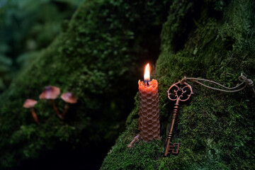 vintage magical key and burning wax candle in mystery dark forest, abstract nature background. wiccan witchcraft, esoteric ritual. mysterious fairy tale scene