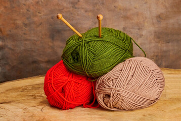 image with three skeins for knitting of different colors with wooden knitting needles in them on a beige background