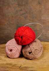 image with three skeins for knitting of different colors with knitting needles in them on a beige background