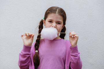 A girl with braids eats cotton candy on a stick in the garden.
