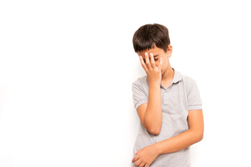 Young boy in a grey polo shirt stands isolated on a white background, covering his face with one...