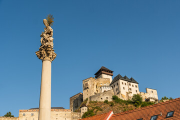 Fototapeta premium Pestsäule zum Gedenken der Opfer der Pest zum Beginn des 18. Jahrhunderts, im Hintergrund ist die Burg Trenčín , Kulturhauptstadt 2026, Trenčín, Slowakei