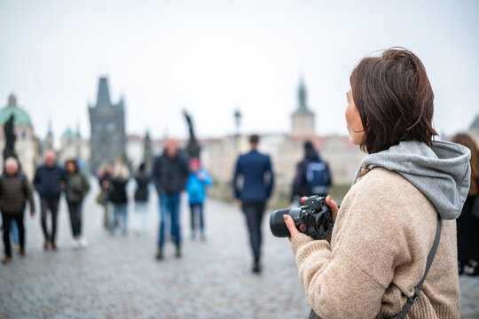 Female Photographer Taking Photos On Charles Bridge In Prague Among The Tourist Crowd