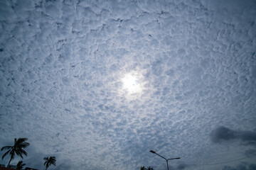   A dramatic sky view showcasing the sun partially obscured by a dense layer of altocumulus clouds,...