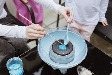 A teenage girl and her sisters spoon blue sugar into a cotton candy machine.