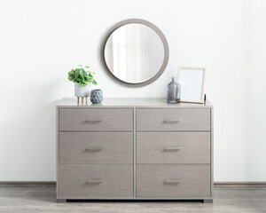 Modern bedroom dresser in light ash wood finish with six flat-panel drawers, sleek silver handles and round wall mirror above, styled with small decorative vases, frame and potted plant for balance.