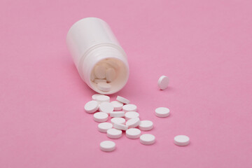 White pills spilled from a bottle on pink background.