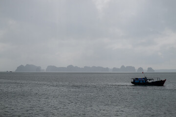 Boats floating on Ha Long Bay in Vietnam with dramatic limestone cliffs and overcast skies.