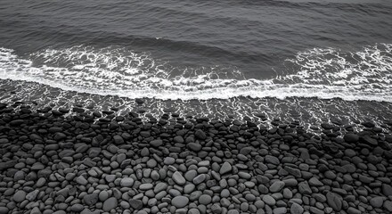 Dramatic coastal landscape of pebbles being lapped by sea waves, Gentle sea foam contrast with grey pebble beach at shoreline