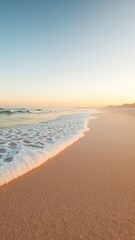 Fototapeta premium Gentle waves washing ashore onto the smooth sand with a gradient sky above, conveying tranquility and a serene coastal atmosphere