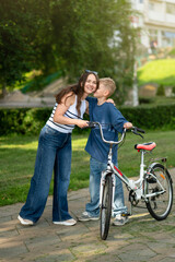 Mother and son standing next to bicycle together in green park on a sunny day