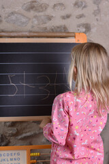 Vertical view of the the girl going mathematical addition and writing on the black chalkboard.