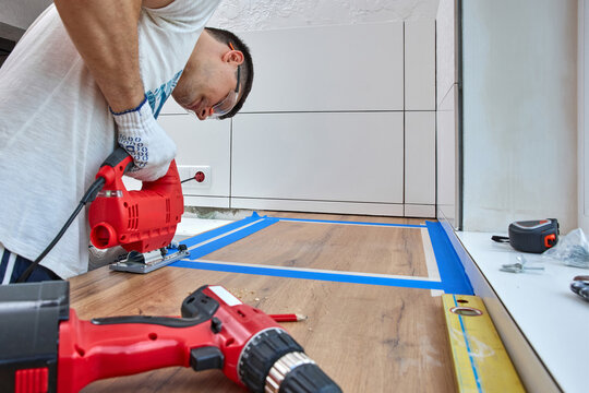 repairman using electric jigsaw and cutting hole for the sink in the kitchen countertops
