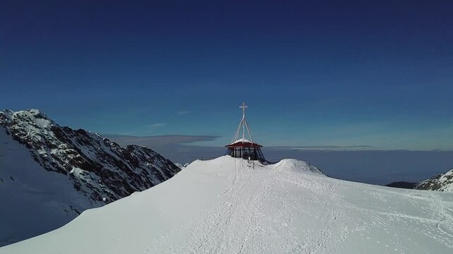 Drone captures Lake B&acirc;lea frozen in snow, flying over snow-covered peaks toward a Christian cross perched on the mountain in wintertime Romania