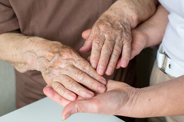 Asian woman doctor consoling senior patient with holding her hand. Private duty nurse visit and take care elderly woman on the bed at home. Home medical caregiving service and health insurance concept