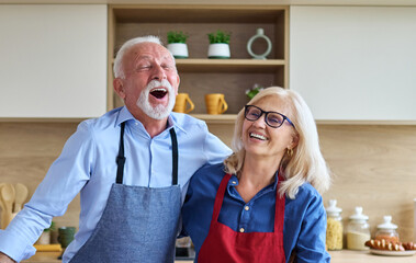 Portrait of happy senior mid aged mature couple prepering meal with fresh vegatebles in kitchen at...