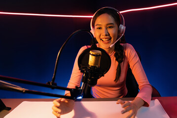 Smiling creative young beautiful Asian influencer talking in channel with positive podcast speech...