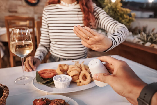 Woman refusing more salt from her partner in a restaurant during dinner with fried calamari, tomato, salad and white wine
