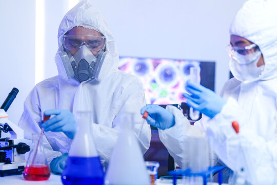 A frontline team of scientists in full protective hazmat suits follows strict protocols in a sterile laboratory. Concept for teamwork, safety, and scientific procedure.